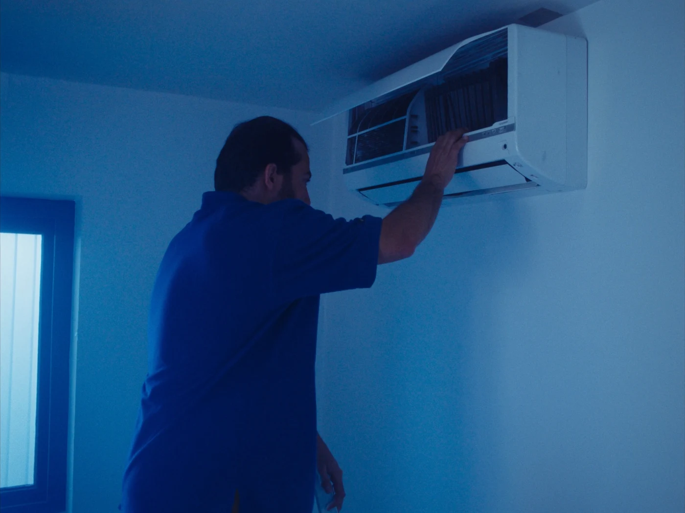 Técnico abrindo a tampa de um ar-condicionado split na parede para limpeza